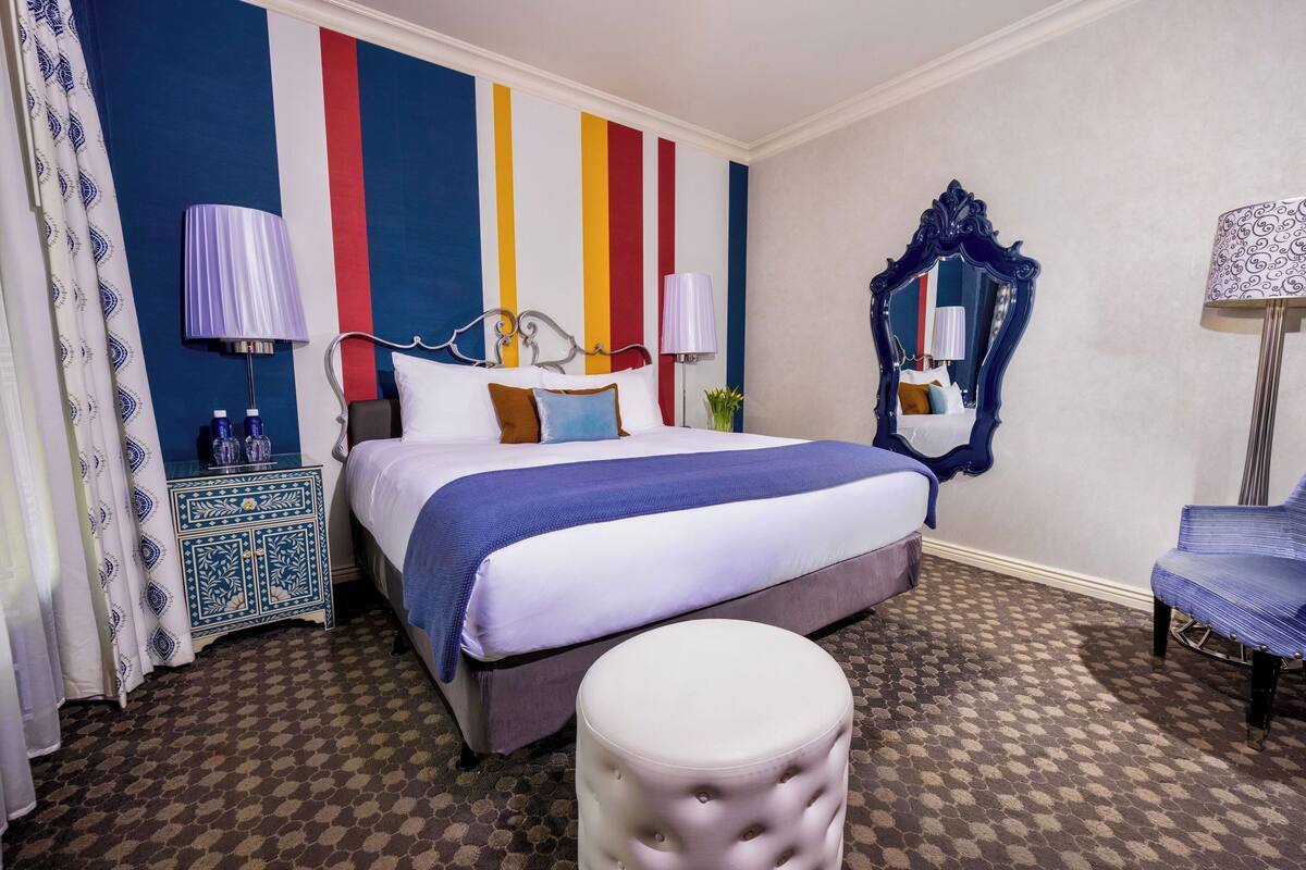 A hotel room with a bed, a nightstand, a mirror, a chair, and a patterned carpet.