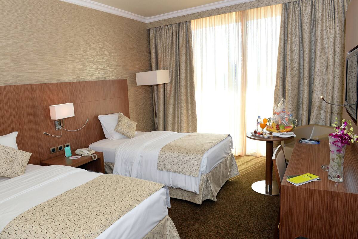 Una habitación de hotel con dos camas, un escritorio, un televisor y una ventana con cortinas.