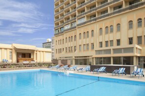 Een hotel met een zwembad, ligbedden en een meerhoog gebouw met balkons.