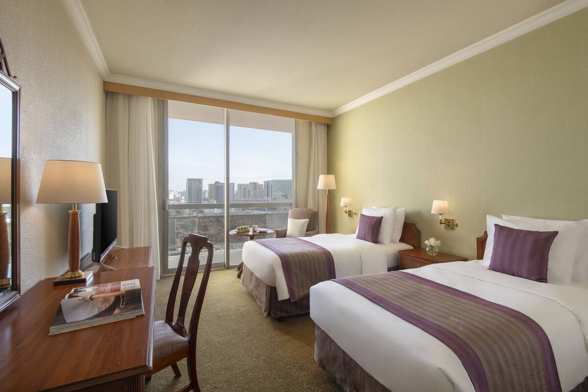 Habitación de hotel con dos camas, un escritorio, una silla y vista a la ciudad.
