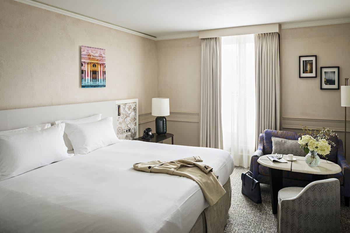 A hotel room with a large bed, a small table with a vase of flowers, a chair, and a sofa.