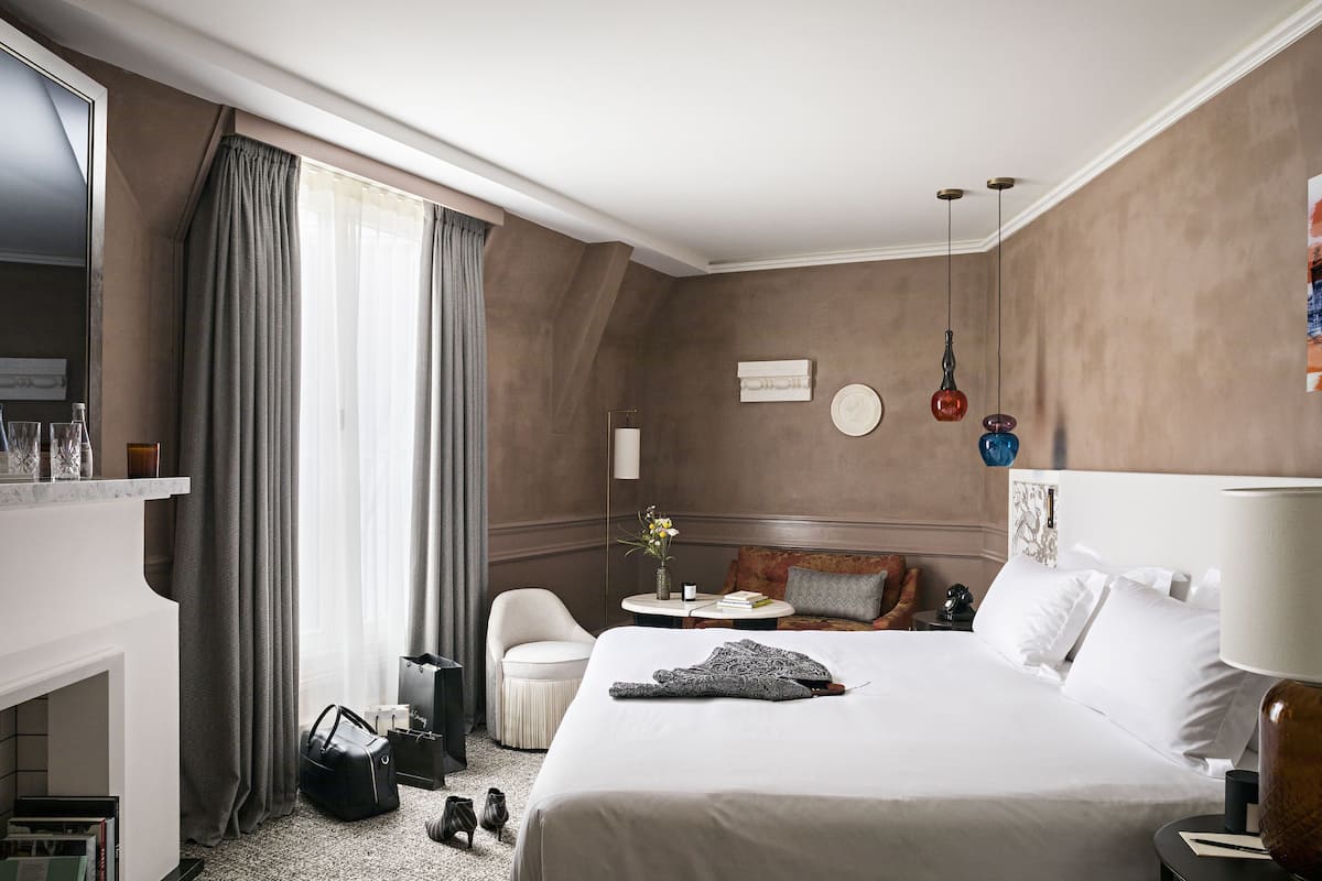 A hotel room with a bed, a desk, a chair, a small table with a vase of flowers, and a wardrobe.