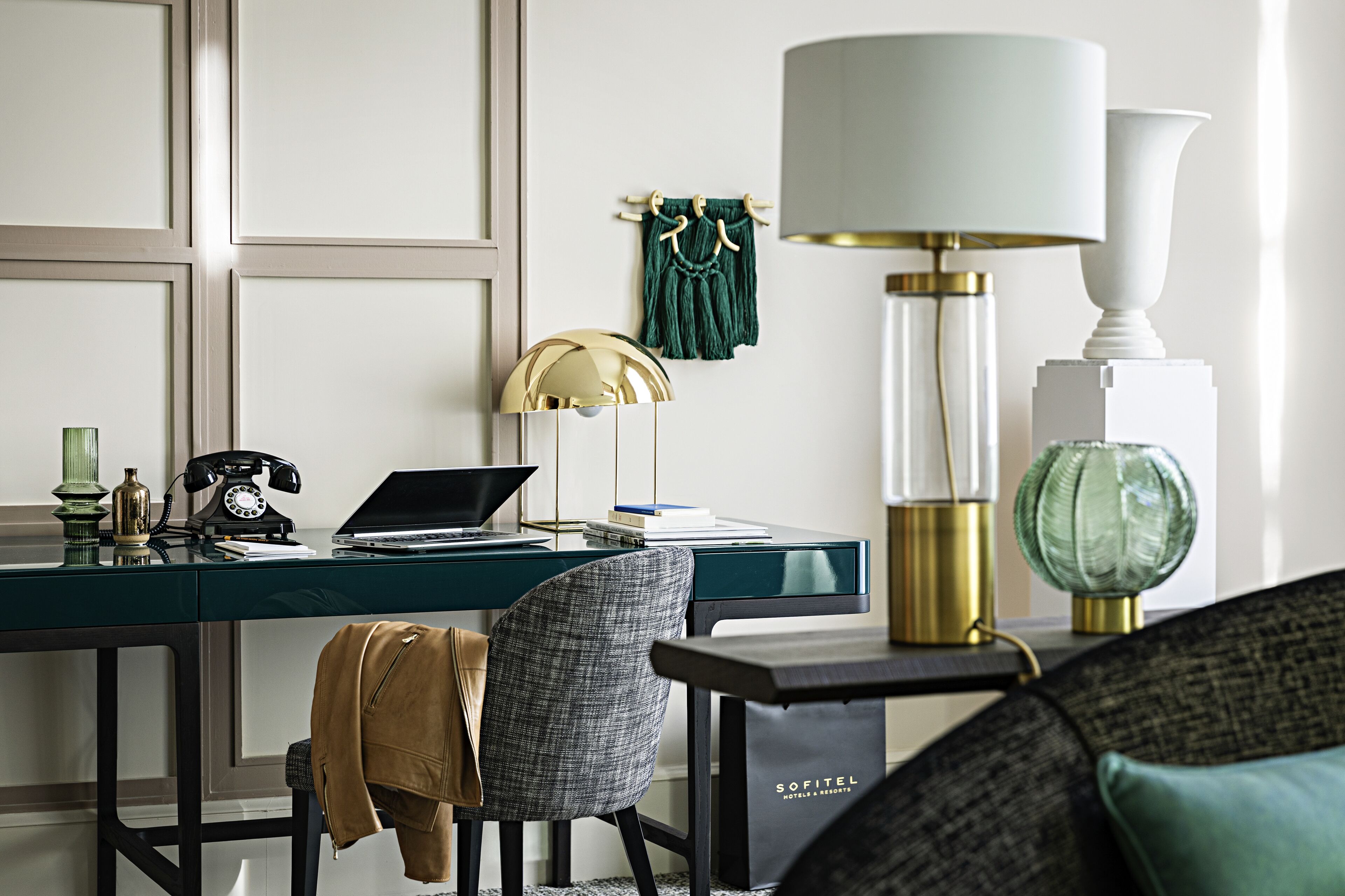 Une chambre d’hôtel moderne avec un bureau vert foncé, un ordinateur portable, un téléphone ancien, une lampe et un canapé.