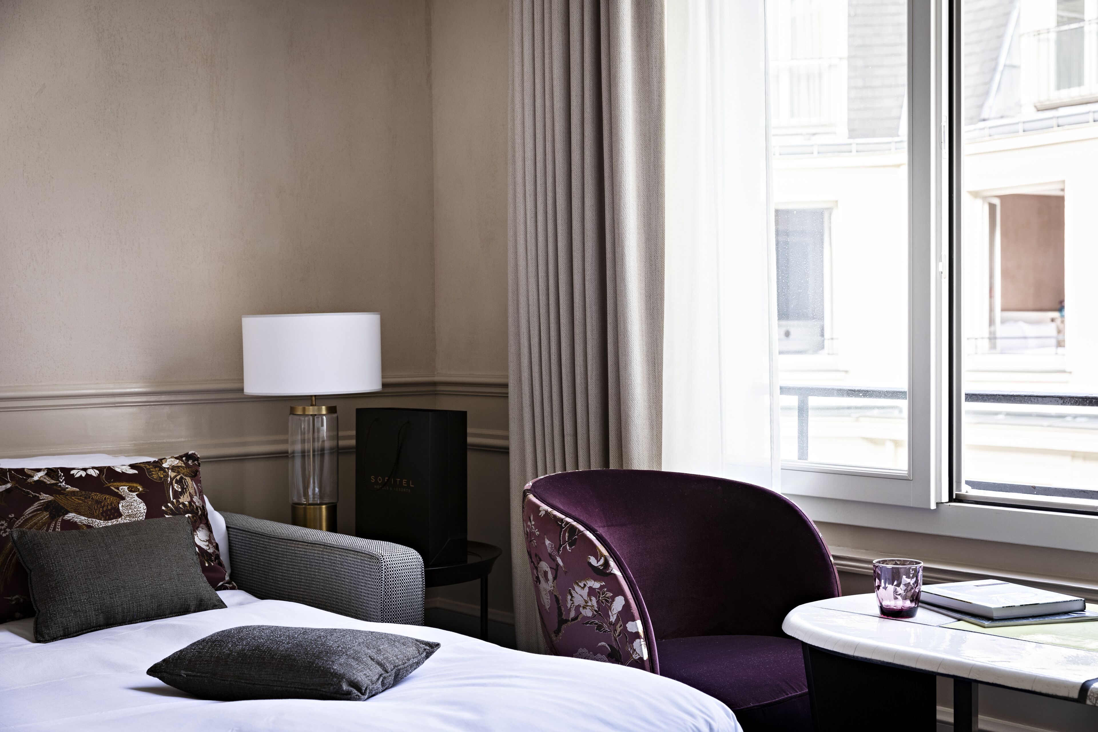 Une chambre d’hôtel avec un lit, une chaise, une table, une lampe et une vue sur l’extérieur.
