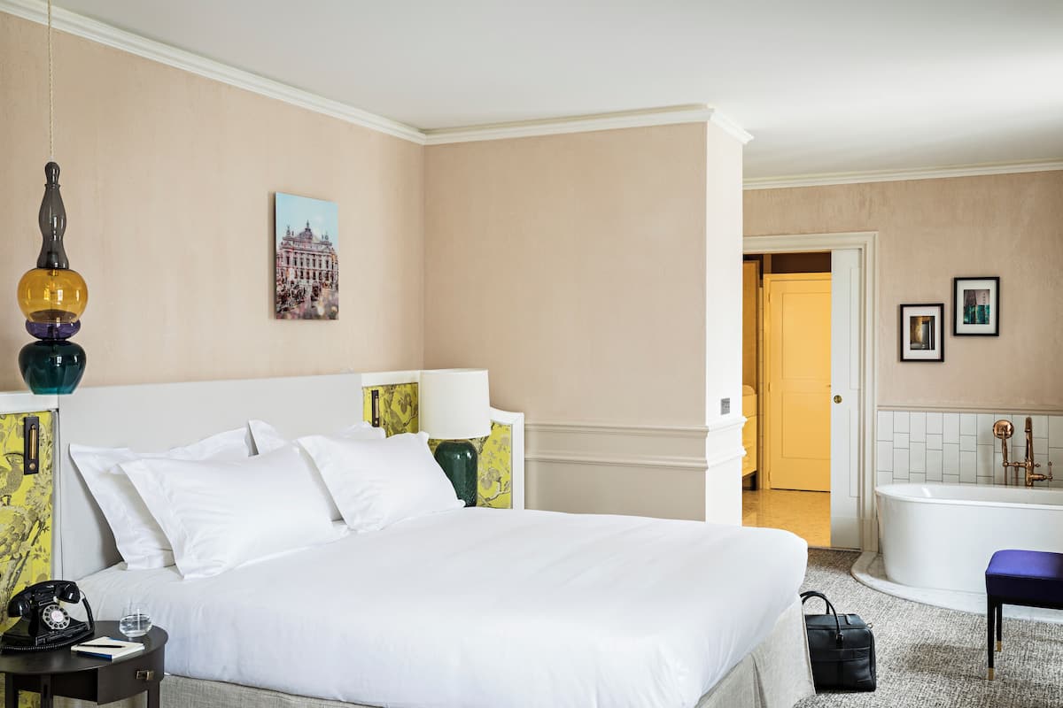 A hotel room with a bed, bedside table, lamp, and a bathroom with a bathtub.