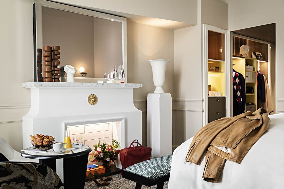 A hotel room with a fireplace, a dining table with breakfast, a mirror, and a wardrobe.