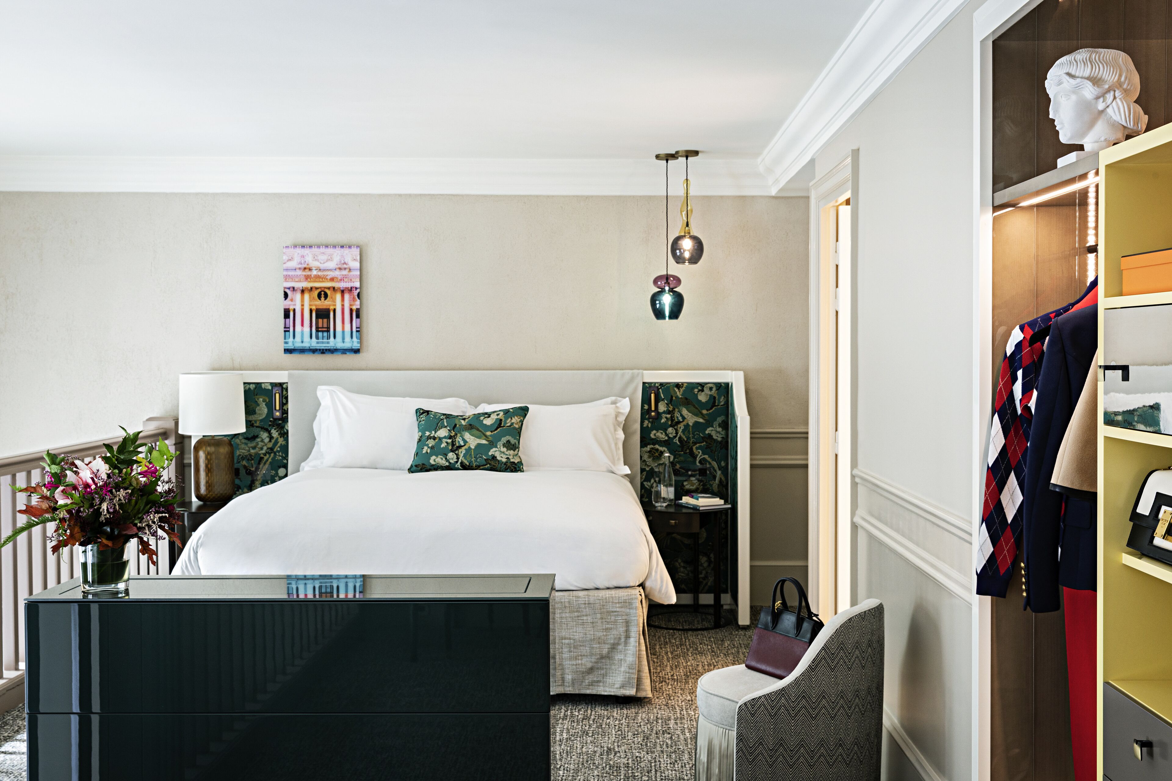 A hotel room with a large bed, a nightstand, a chair, a wardrobe, and a painting on the wall.