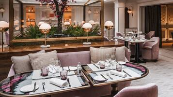 A dining area with a glass table, pink upholstered chairs, and a central floral arrangement.