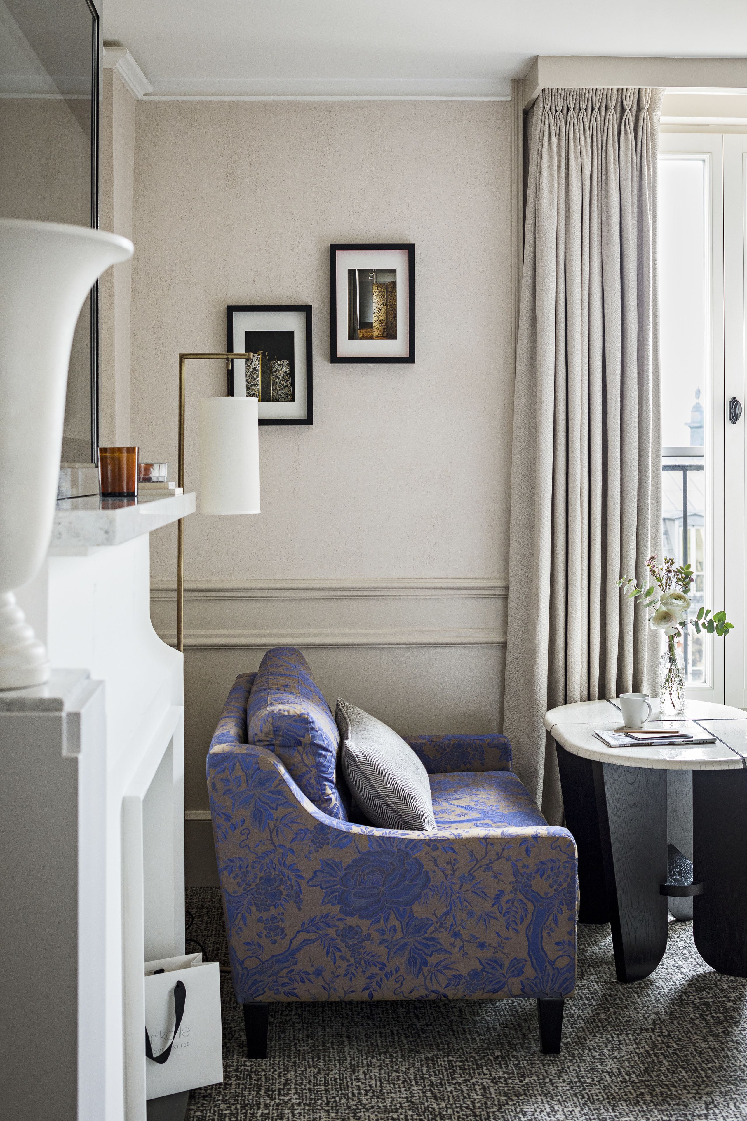 Una habitación de hotel moderna con un sofá azul estampado, una lámpara blanca y una mesita auxiliar con un jarrón.