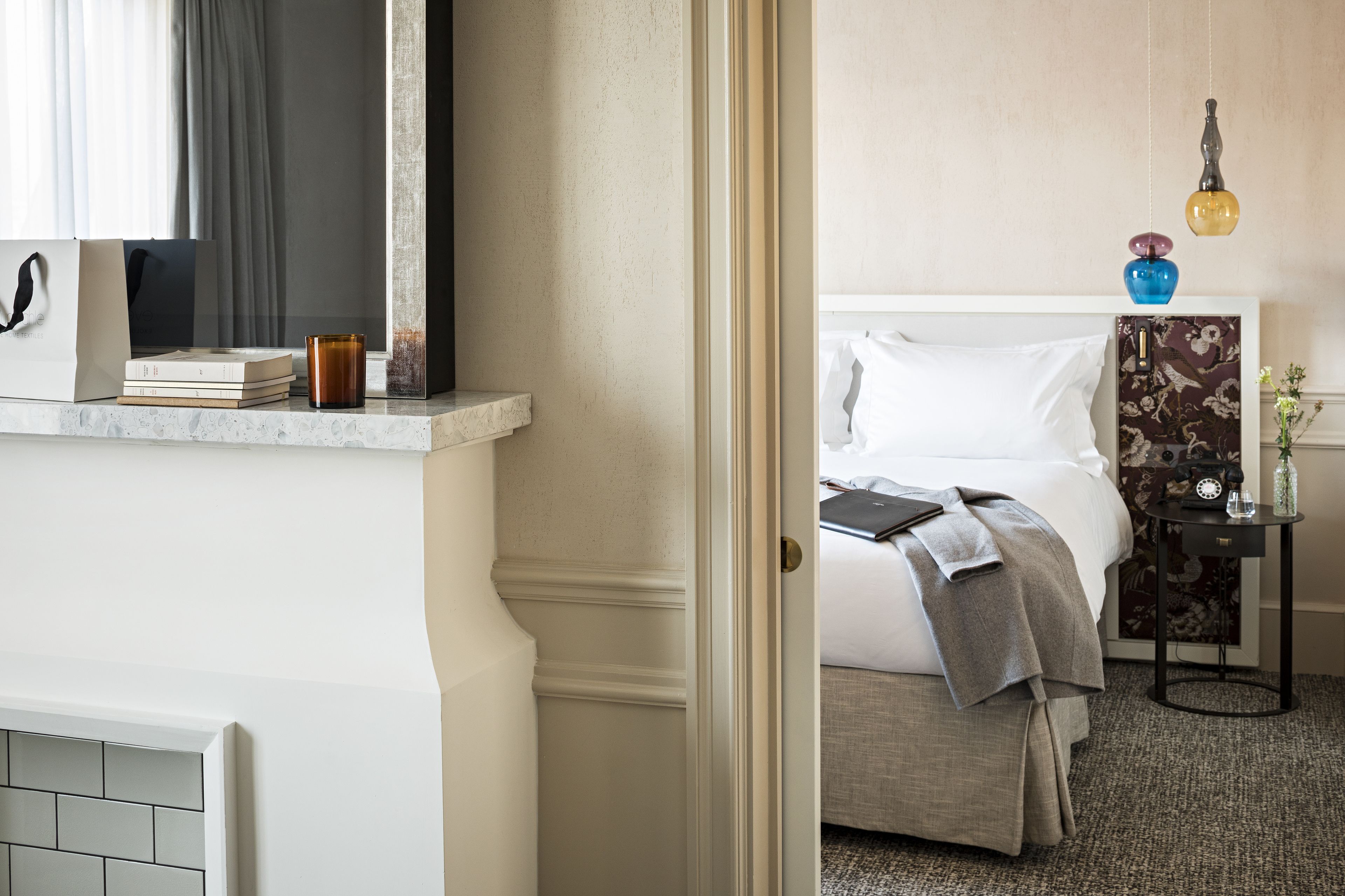 A hotel room with a bed, bedside table, and a small table with a lamp.