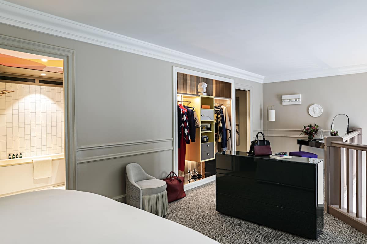 A hotel room with a bed, a desk with a chair, a wardrobe, and a bathroom with a bathtub and towel.