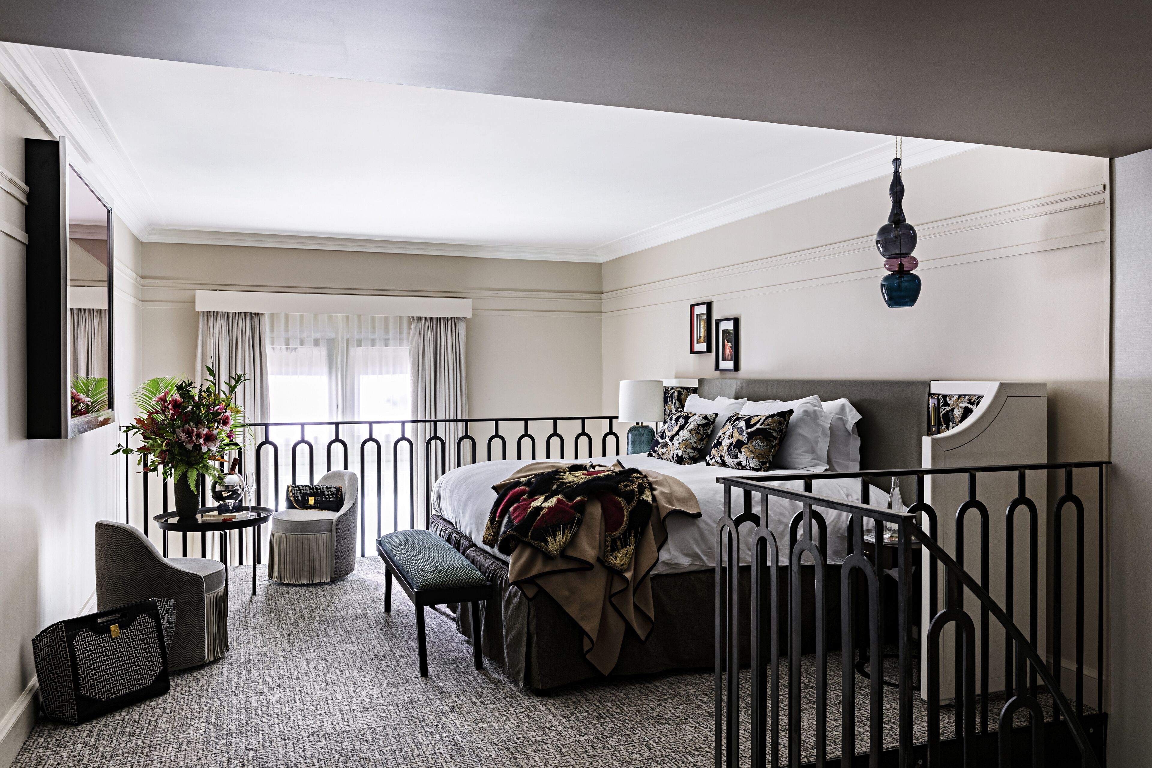 A bedroom with a bed, bedside tables, a bench, a potted plant, and a view of the outside.