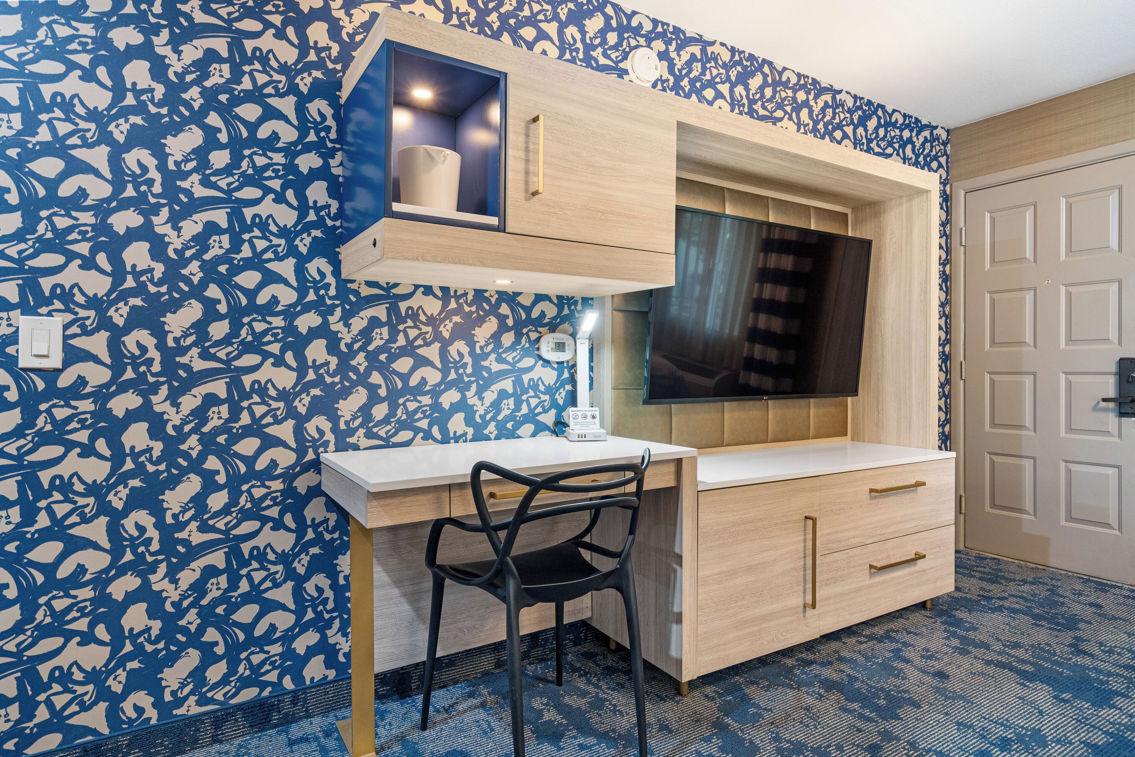Ein Zimmer mit Schreibtisch, Stuhl und einem an der Wand montierten Fernseher.