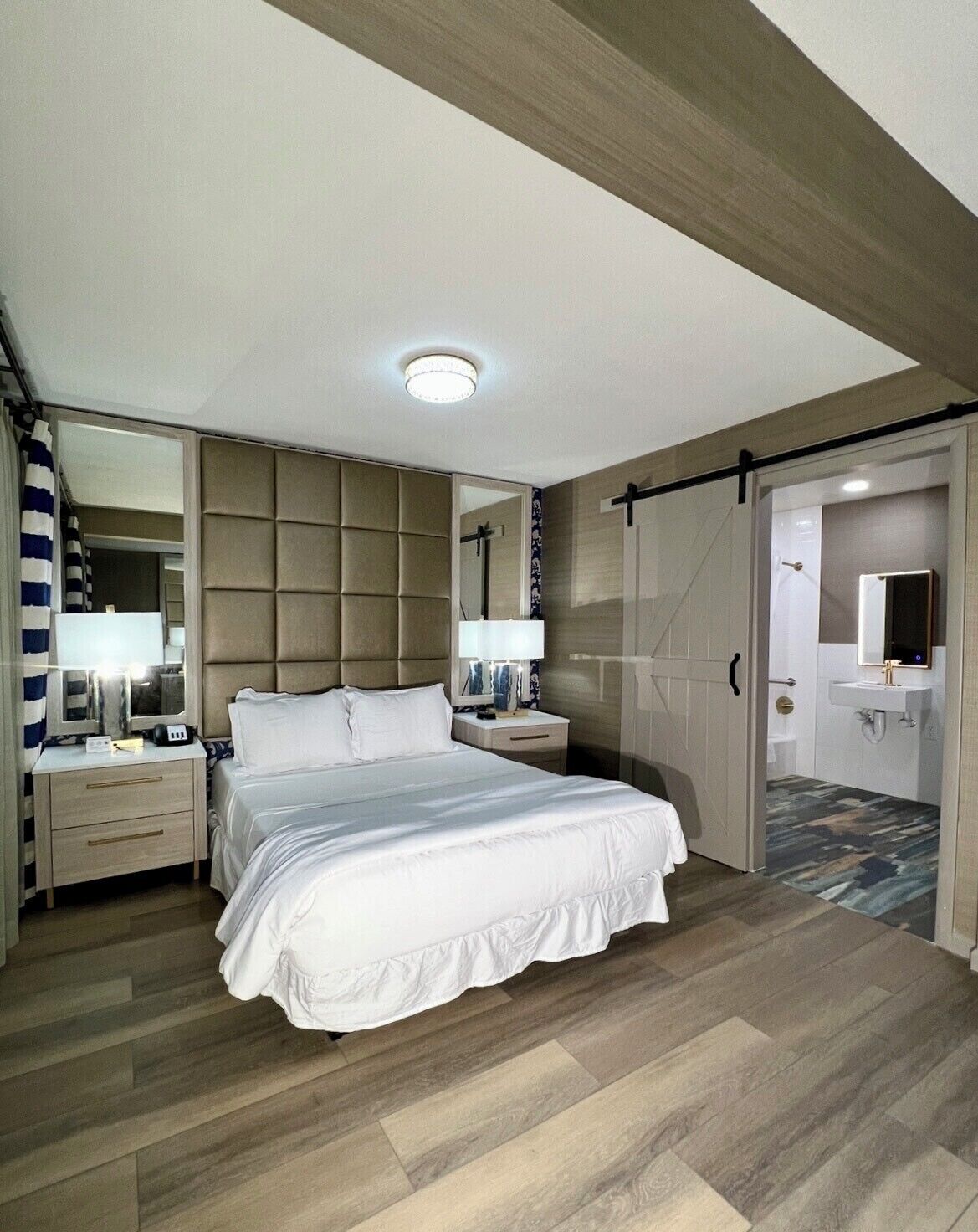 A modern bedroom with a large bed, a bedside table, a mirror, and a wardrobe.