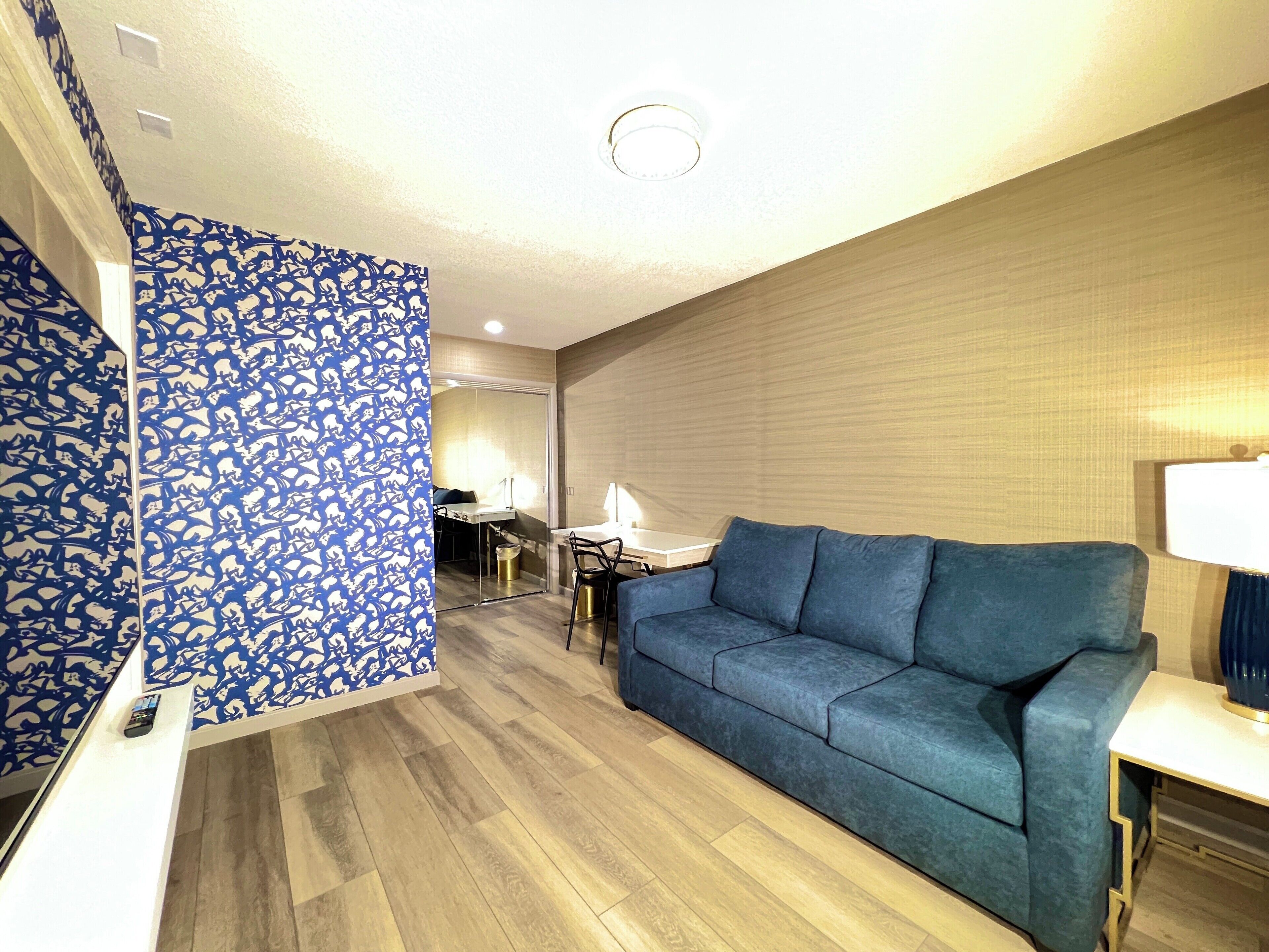 Una sala de estar moderna con una pared azul estampada, un sofá azul y un comedor con mesa y sillas.