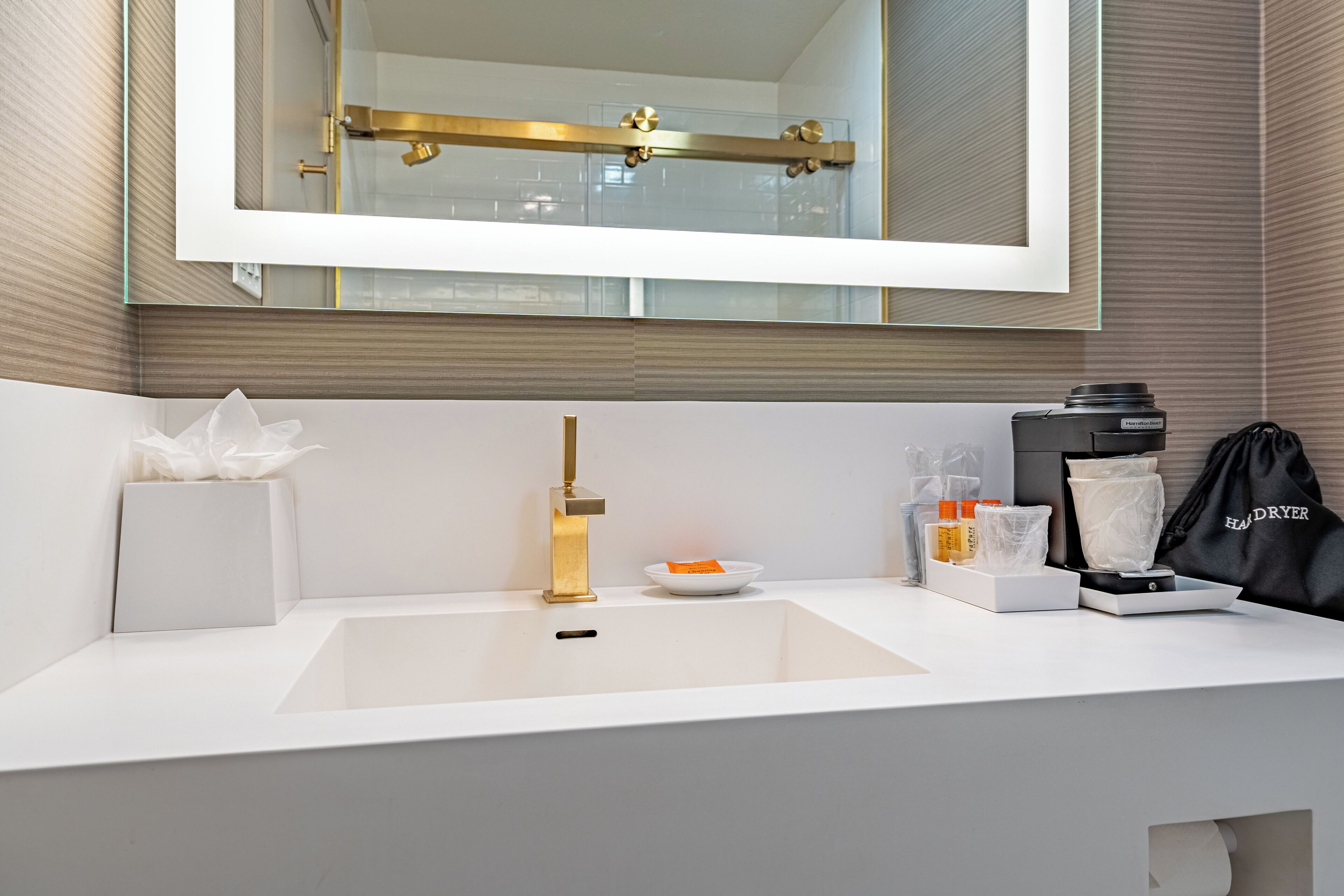Un baño moderno con un lavamanos blanco, grifo dorado y un espejo grande arriba.
