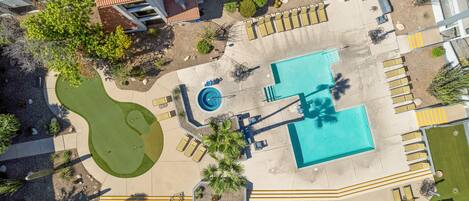 An aerial view of a hotel with a swimming pool, sun loungers, and a small putting green.
