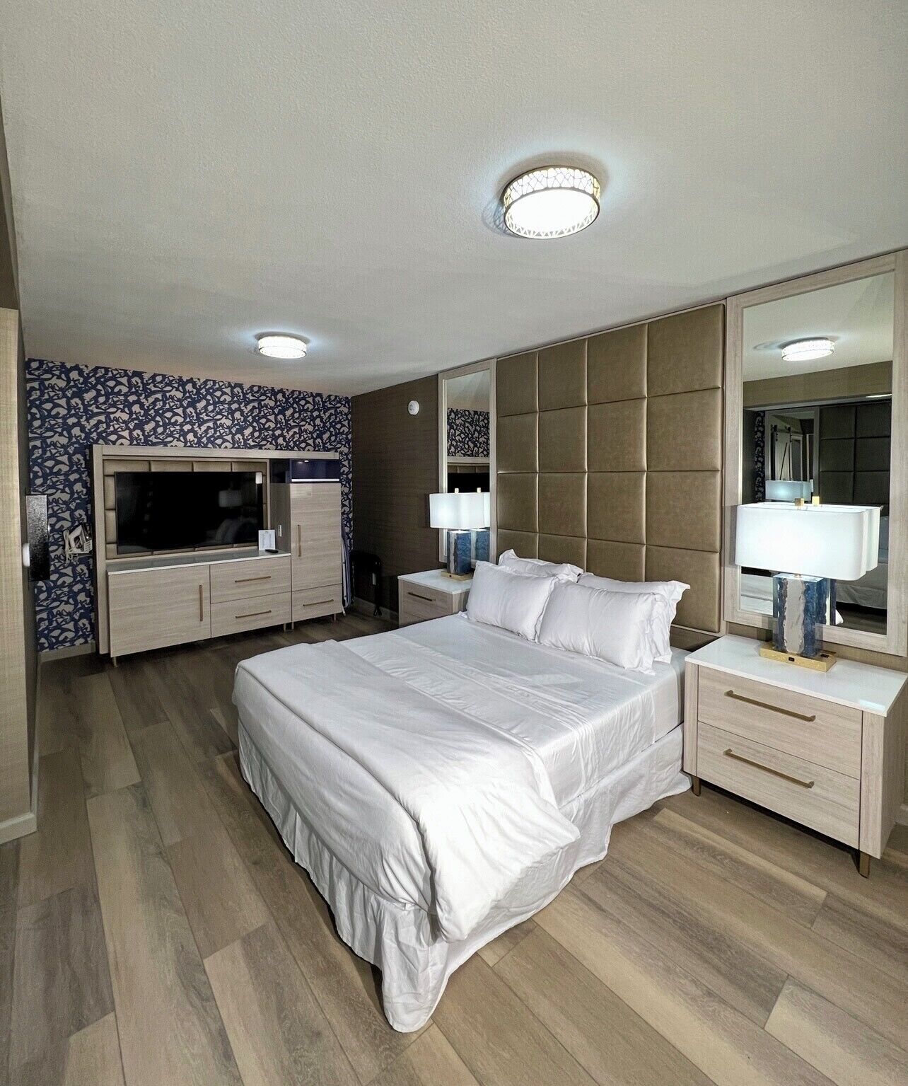 A modern hotel room with a large bed, a TV, a wardrobe, and a mirror.
