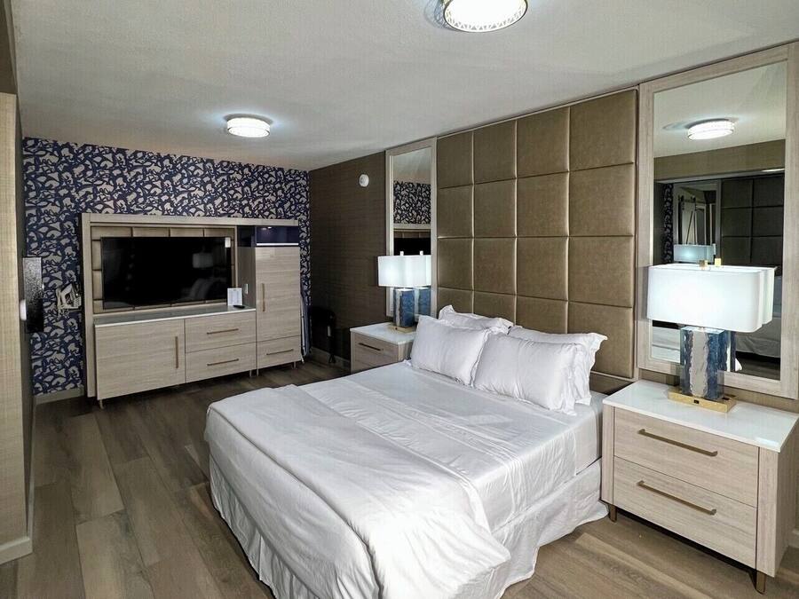 A modern hotel room with a large bed, a TV, a wardrobe, and a mirror.