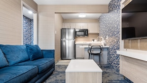 A compact living space with a sofa, a small table, a kitchen area with a refrigerator and microwave, and a TV mounted on the wall. - 3 Palms Tucson North Foothills (Tucson)