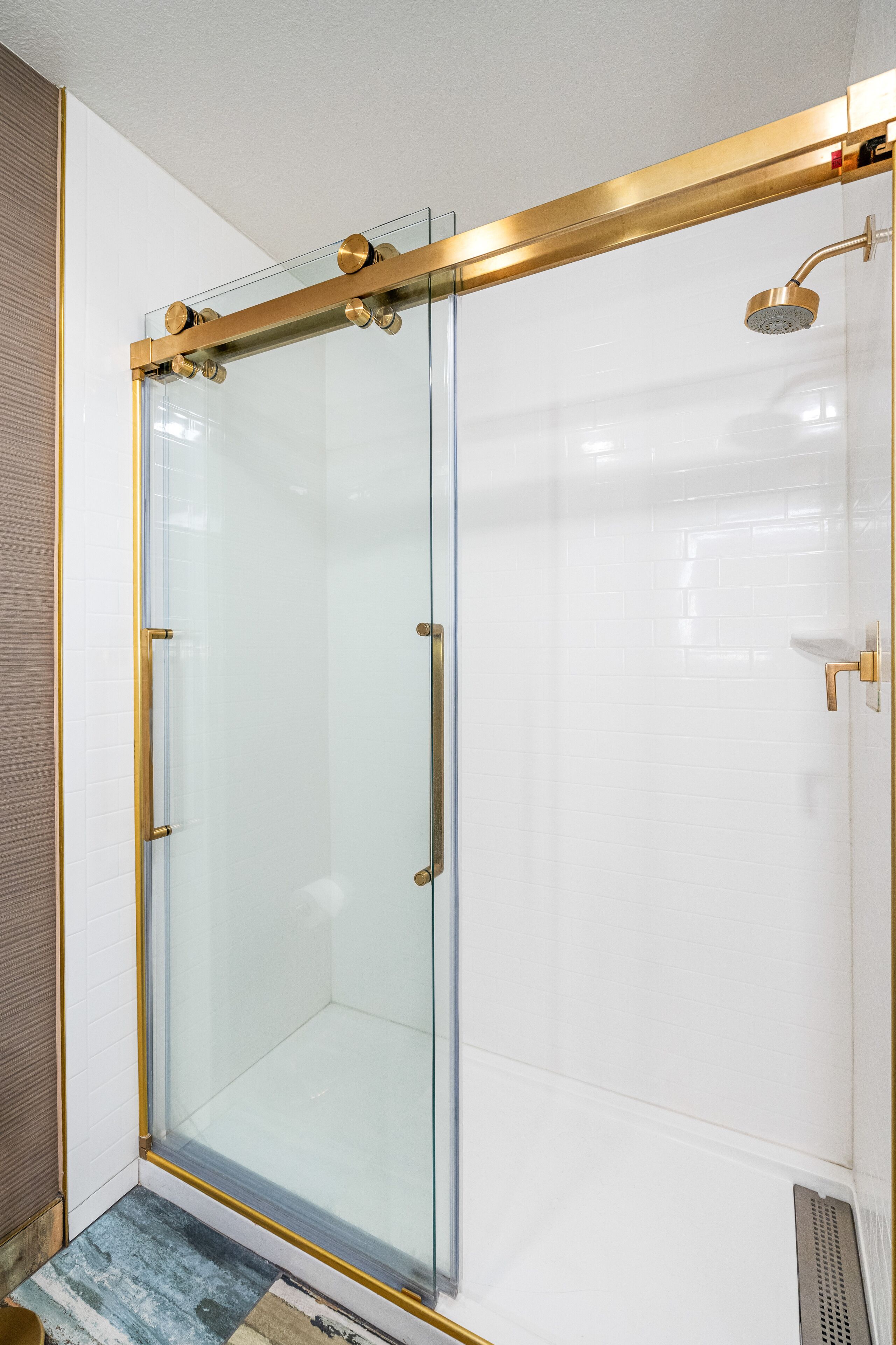 Une douche fermée par des parois en verre, dotée d’un cadre doré et d’un pommeau de douche amovible.