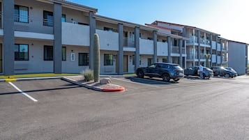 Un hotel de varios pisos con un estacionamiento, varios coches y un cactus en primer plano.