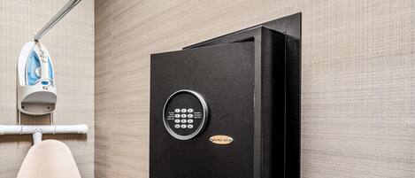 A wall-mounted safe with a keypad lock, a hanging iron, and a towel rack in a hotel room.