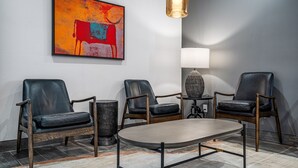 A modern lounge with leather chairs, a round table, a lamp, and a colorful abstract painting on the wall. - 3 Palms Tucson North Foothills (Tucson)