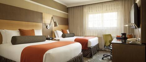 A hotel room with two beds, a desk, a chair, a TV, and a window with curtains.
