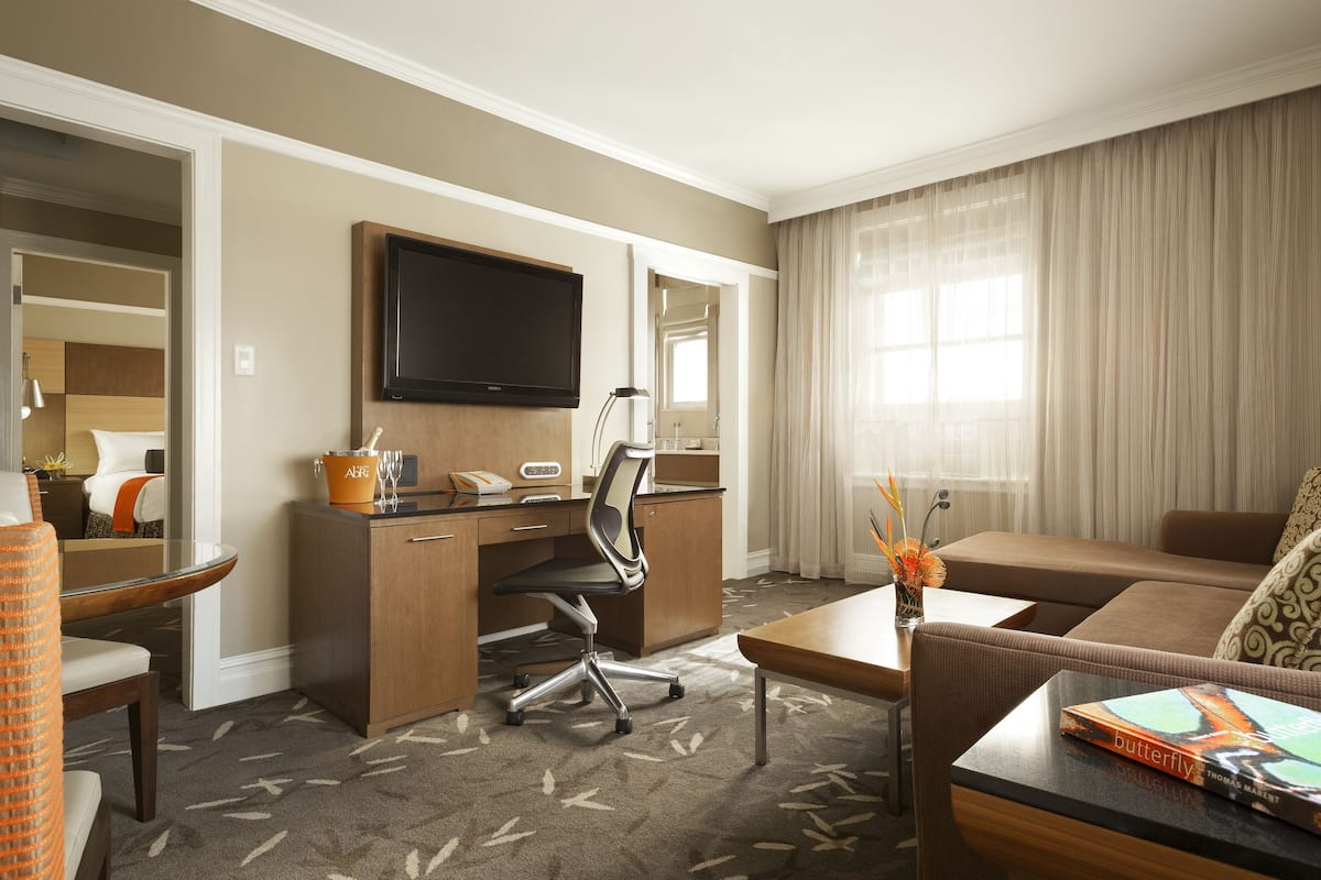 A hotel room with a desk, chair, sofa, and a TV mounted on the wall.