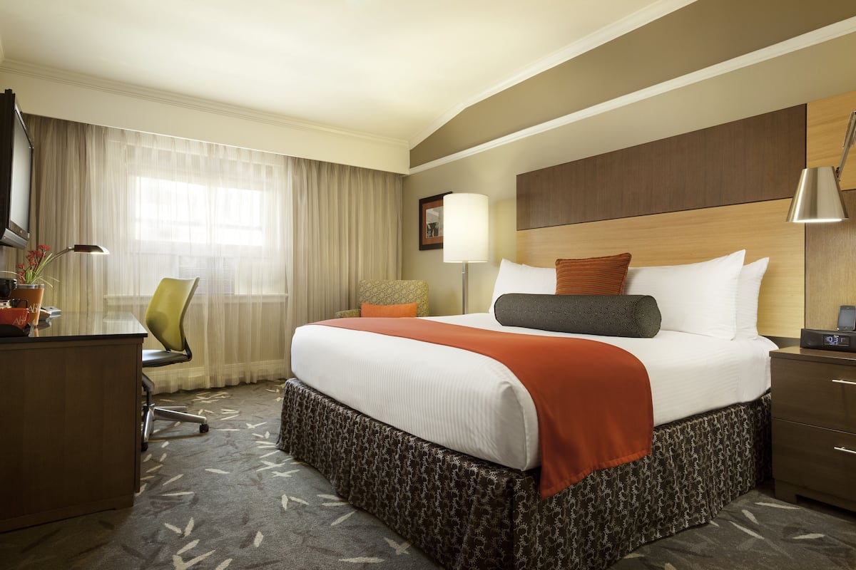 A hotel room with a large bed, a desk, a chair, a lamp, and a window with curtains.