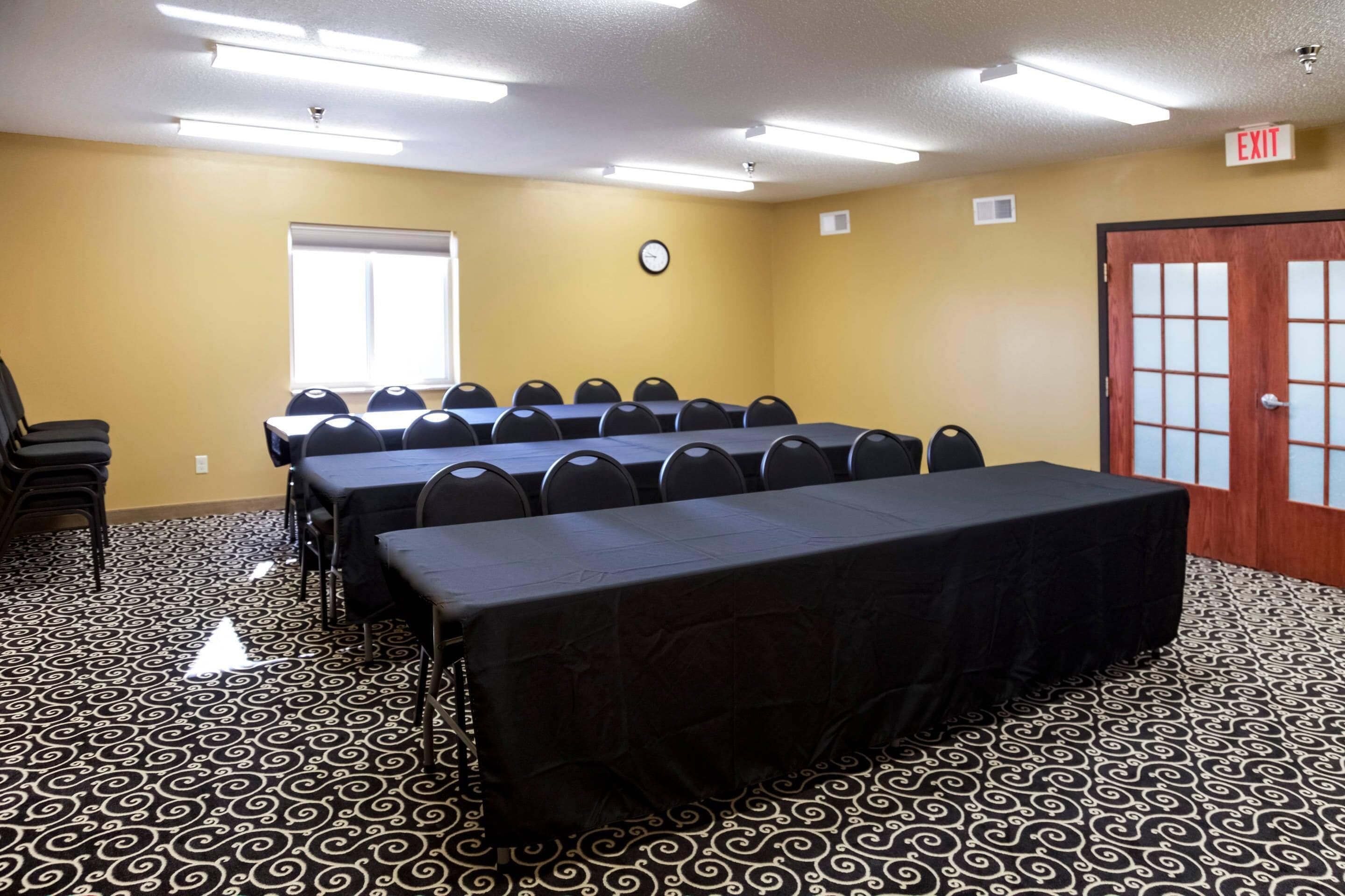 A conference room with a long table, chairs, a clock, and an exit door.