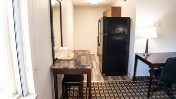 Une chambre d’hôtel compacte comprenant un coin cuisine, une petite table à manger, une chaise, un réfrigérateur et une lampe.