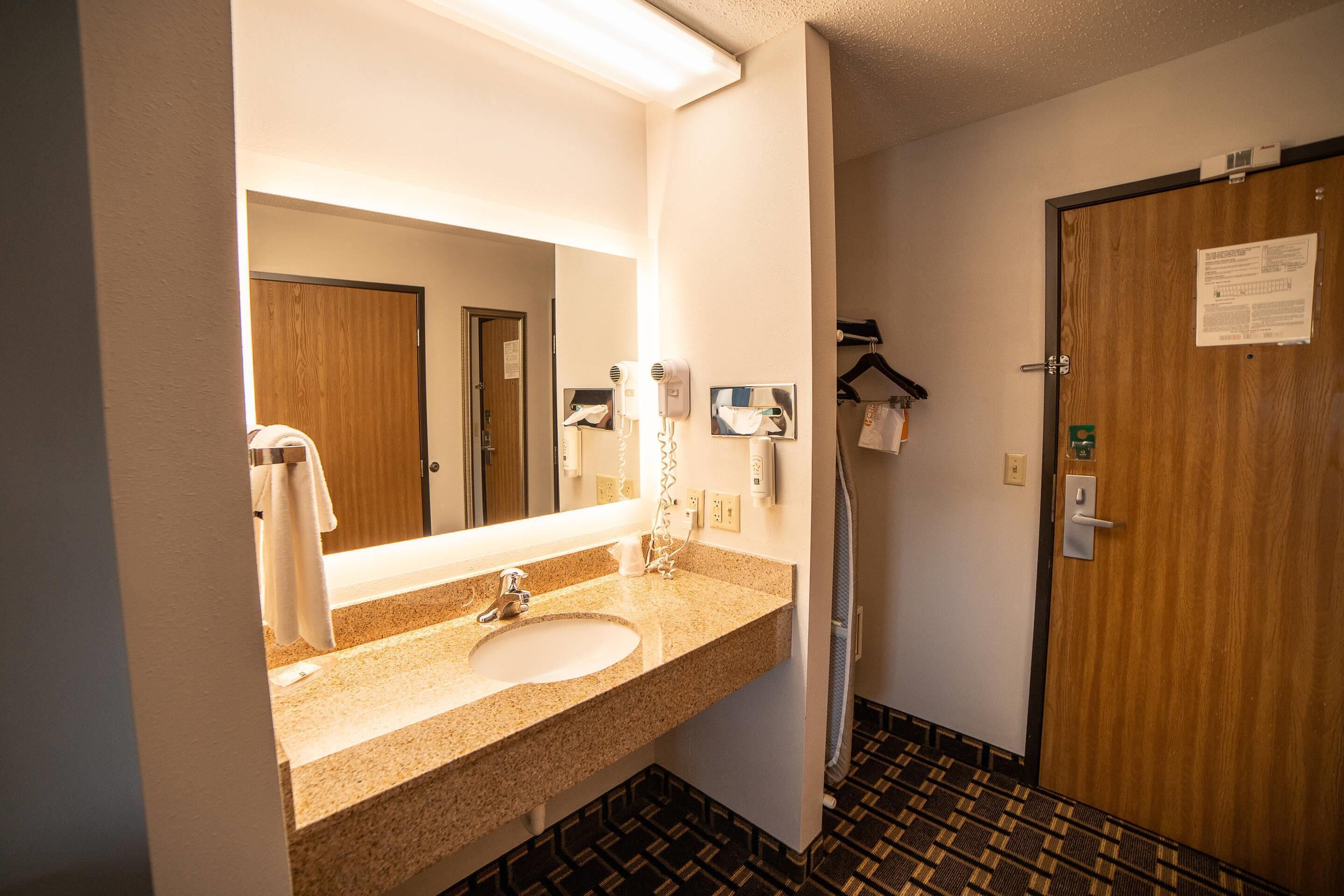 Un baño de hotel con lavamanos, espejo, secador de pelo y toallero.