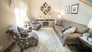 A living room with patterned armchairs, a sofa, a coffee table, a rug, a console table with decorative items, and a staircase. - Quality Inn & Suites Watertown near Prairie Lakes Ice Arena (Watertown)