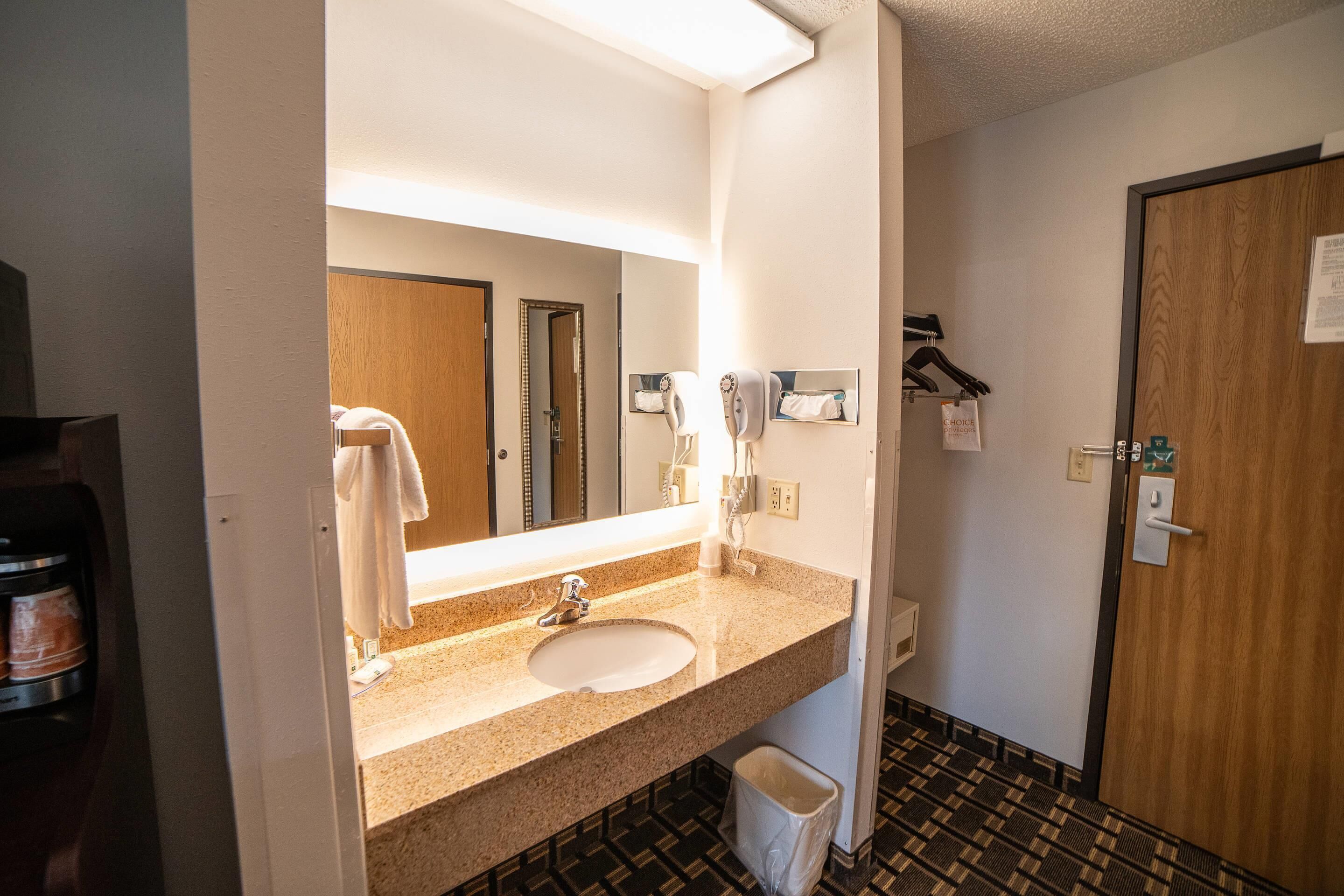 A hotel bathroom with a sink, mirror, towel rack, and a door.