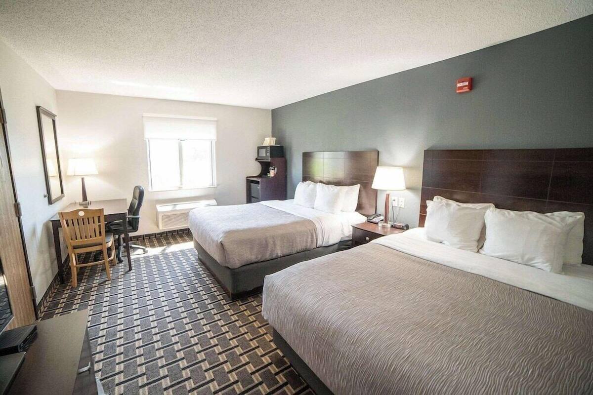 A hotel room with two beds, a desk, a chair, a TV, and a window.