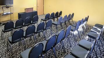 Une salle de conférence avec des rangées de chaises, un pupitre et un téléviseur posé sur un support.