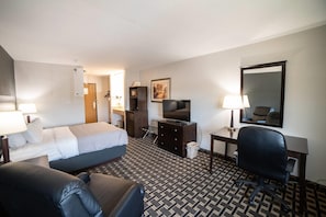 Una habitación de hotel con cama, escritorio, silla, televisor y espejo.