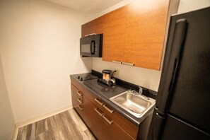 A compact kitchen with a microwave, coffee maker, and stainless steel sink.