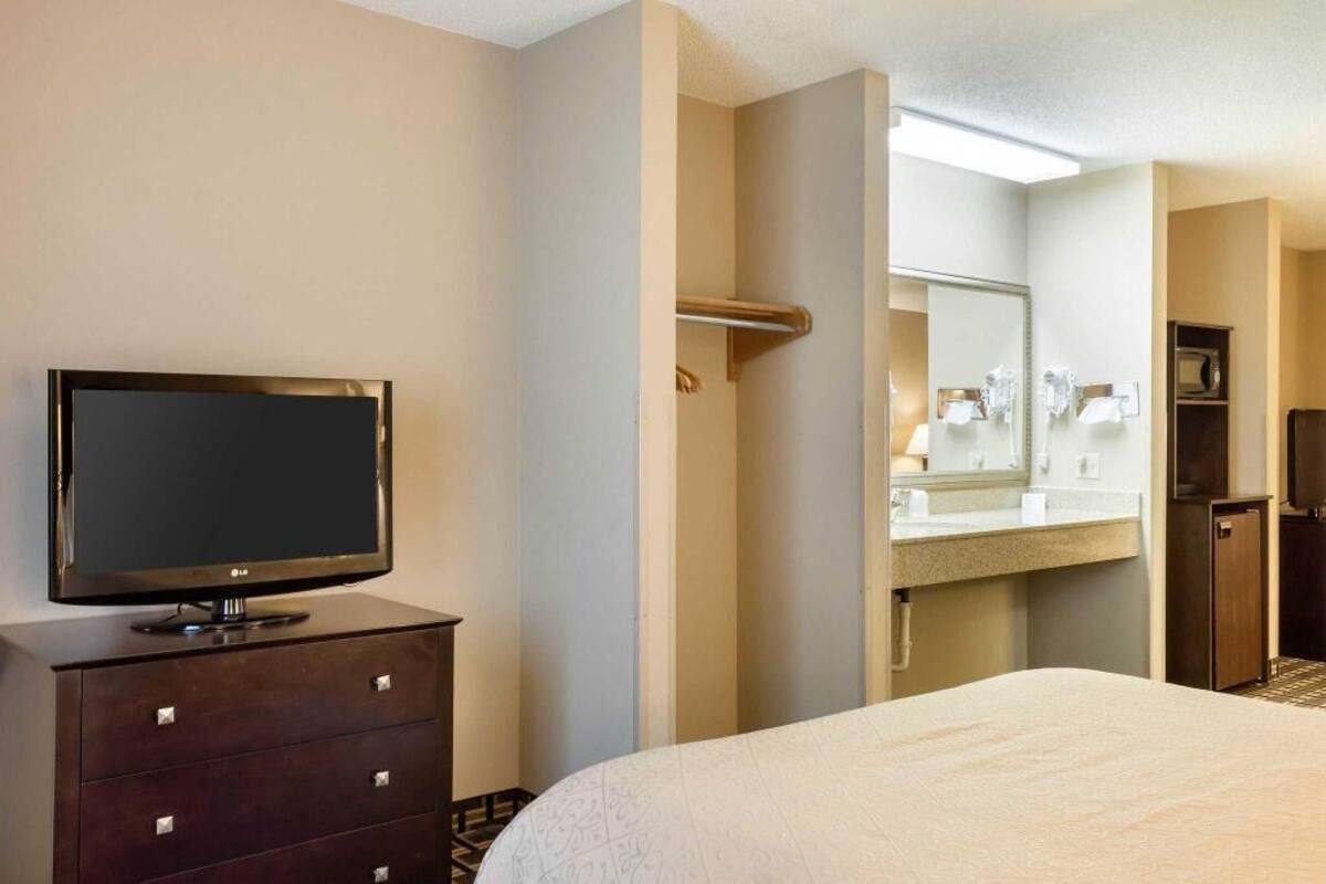 A hotel room with a bed, a TV on a dresser, a bathroom with a mirror, and a sink.