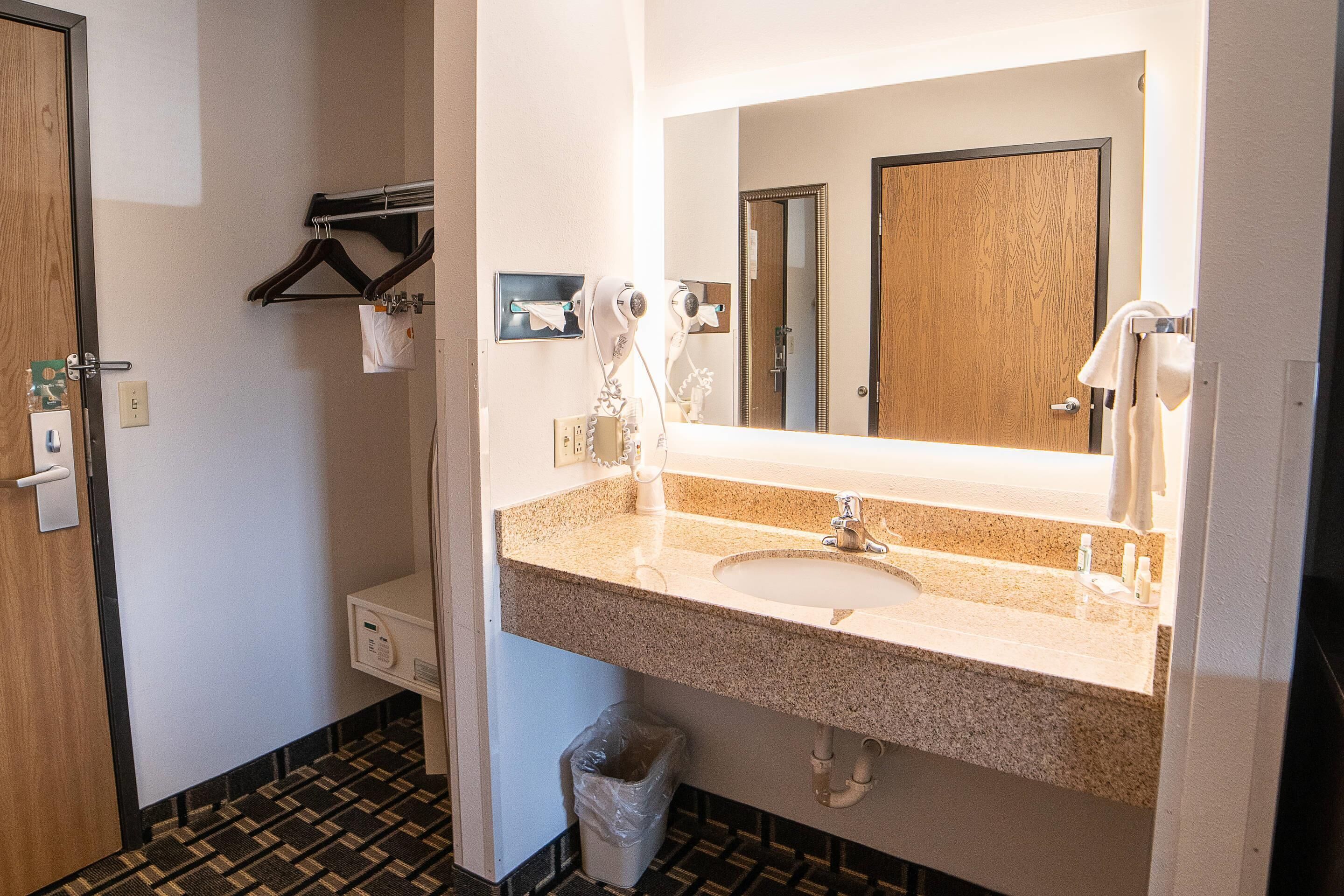 A hotel bathroom with a sink, mirror, towel rack, and a trash bin.