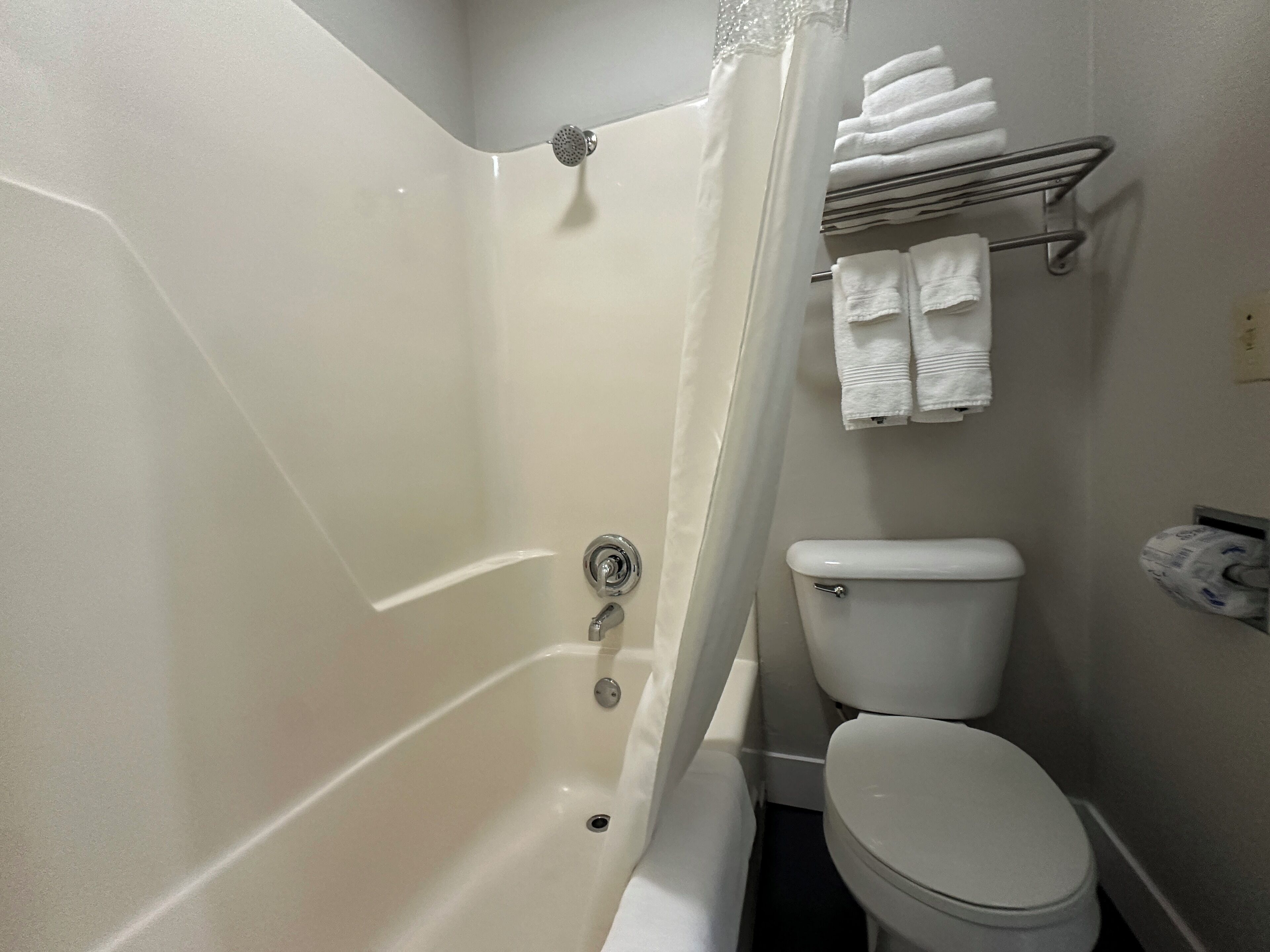 A bathroom with a bathtub, toilet, and a towel rack with folded towels.
