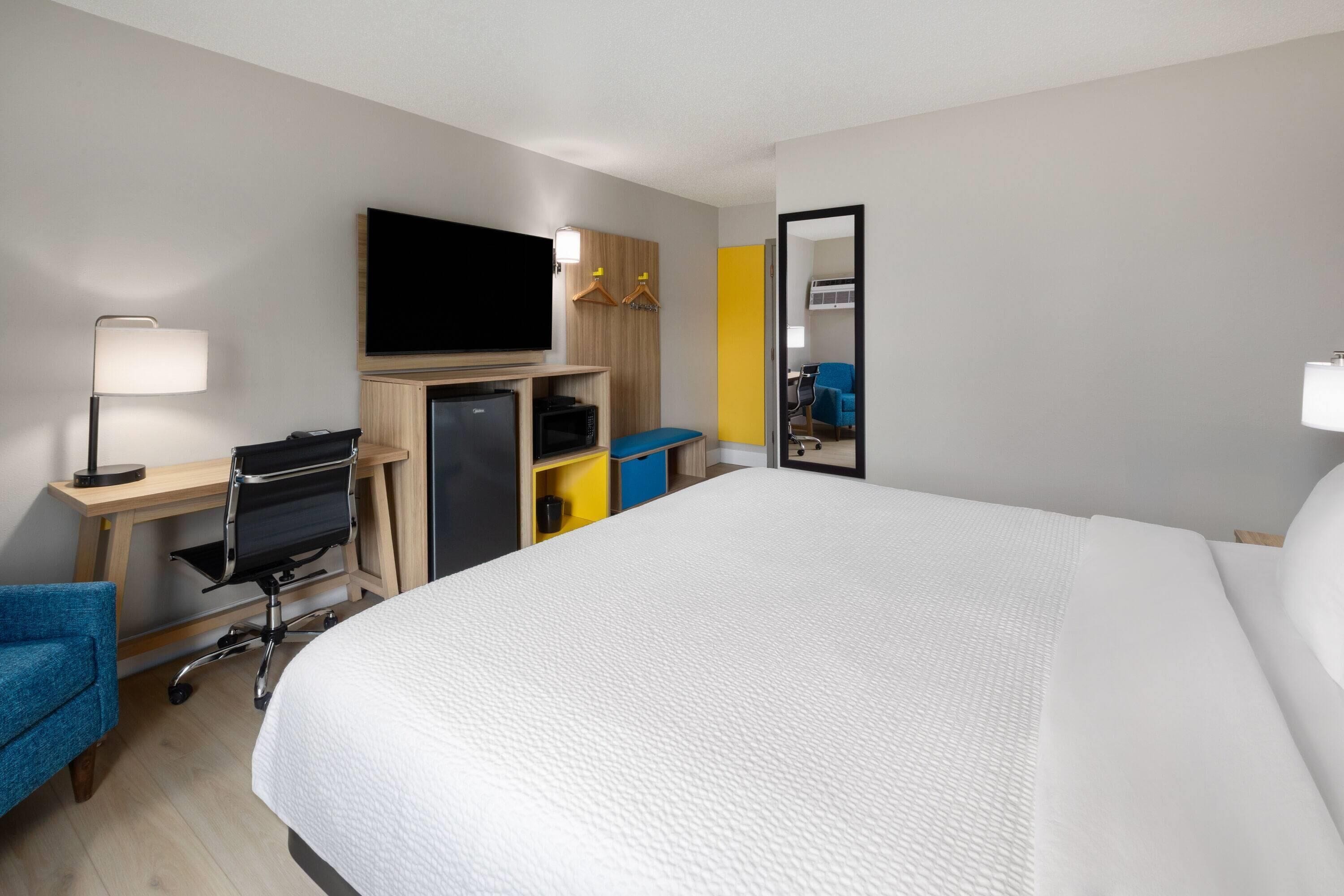A hotel room with a bed, desk, chair, TV, and a mirror.