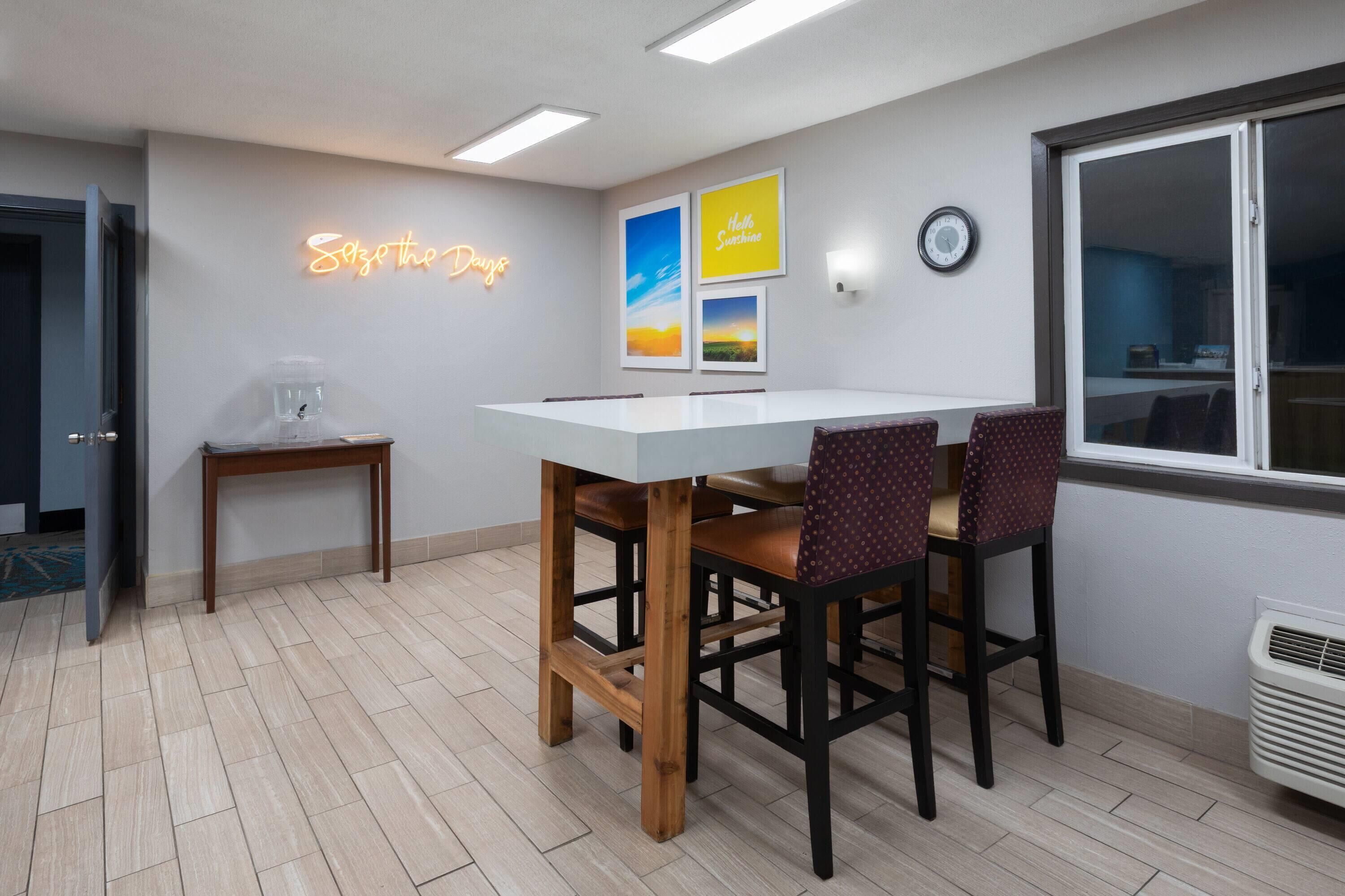 A modern dining area with a white table, wooden chairs, a coffee machine, and wall art.