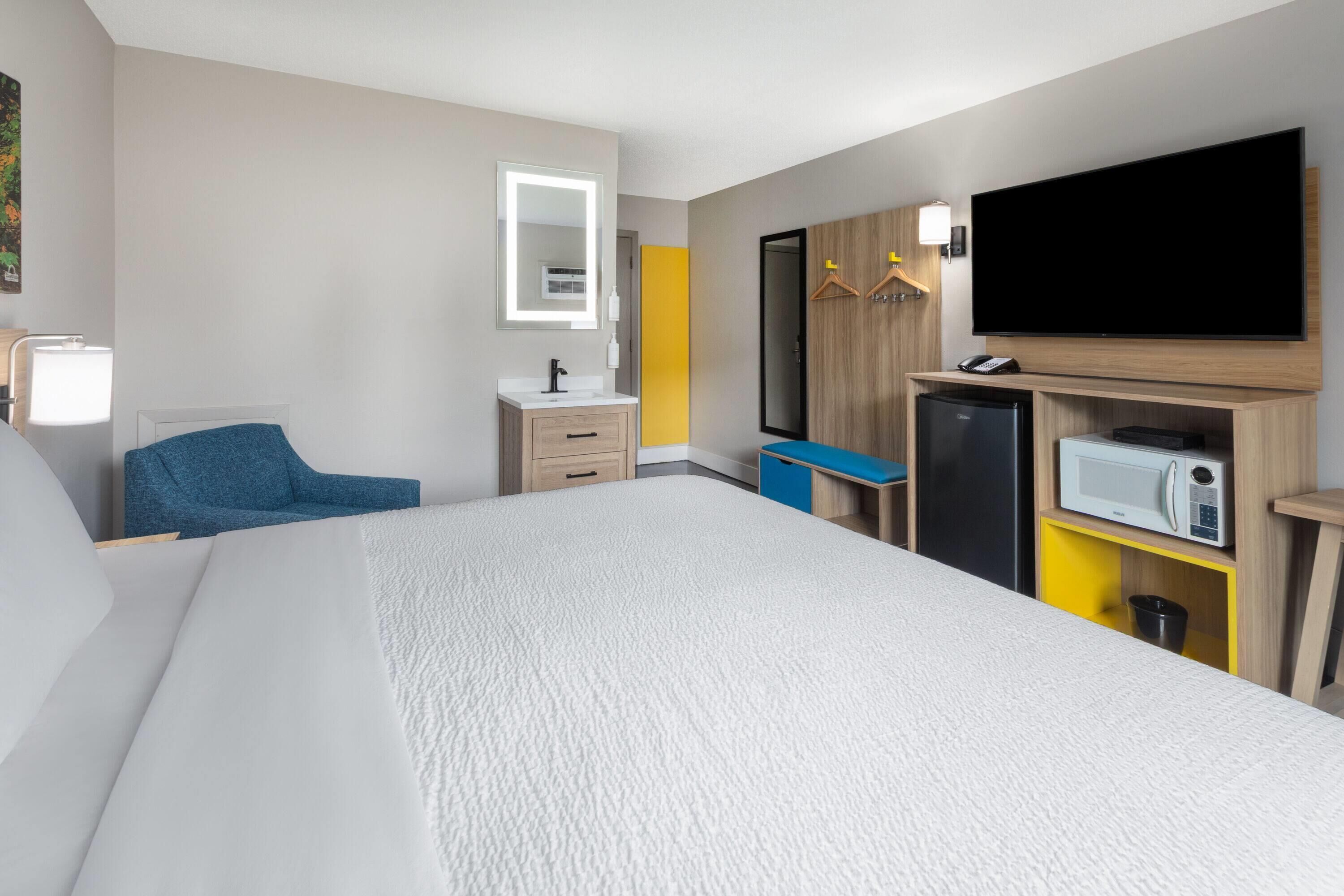 A hotel room with a large bed, a TV, a microwave, a mini-fridge, a desk, and a chair.