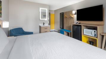 A hotel room with a large bed, a TV, a microwave, a mini-fridge, a desk, and a chair.