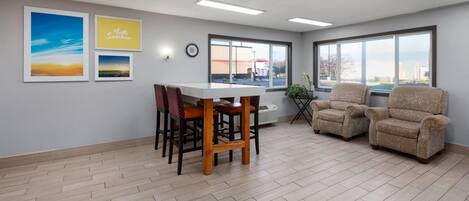 A room with a wooden floor, a table with chairs, two armchairs, and large windows with a view.