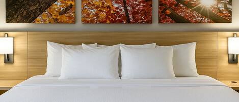 Una habitación de hotel con una cama grande, dos lámparas fijadas a la pared y tres cuadros con hojas de otoño.