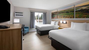 Een hotelkamer met een bed, een bureau, een stoel, een televisie, een airconditioner, een raam met gordijnen en een schilderij aan de muur.